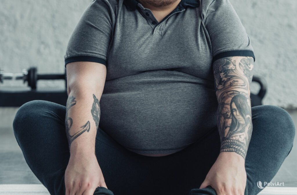 Hombre adulto con sobrepeso sentado en el piso, de espaldas, en postura reflexiva, representando hipogonadismo masculino y salud metabólica