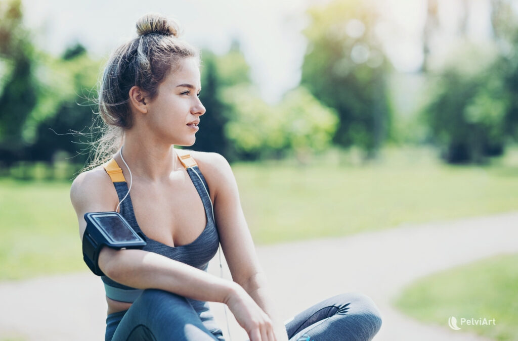 Mujer deportista sentada en el parque después de entrenar, en pausa de recuperación, representando el manejo de síntomas de vejiga hiperactiva en el deporte